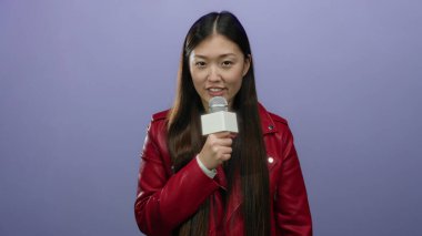 Mikrofona konuşan bir kadın izole edilmiş mor arka planda kırmızı ceket giymiş, kendine güvenen ve ifade veren bir kadın..