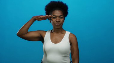 Mavi arka planda beyaz bluz giyen, güçlü pozlar veren bir kadın..