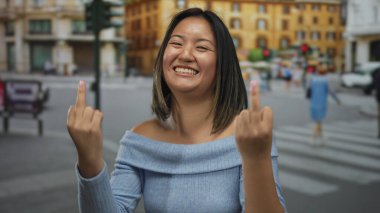 Şehirli bir sokakta neşeli bir jest yaparken gülümseyen bir kadın. Bulanık bir arka plan ve uzaklarda yürüyen insanlar..