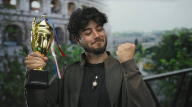 Sakallı genç adam, güneşli bir günde Roma Kolezyumu 'nun yanında mutlu bir şekilde zafer ve heyecan sunuyor..