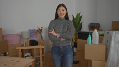 Kendine güvenen bir kadın, etrafı kutularla çevrili yeni bir eve yerleşmenin heyecanını kucaklarken, parlak bir oturma odası sahnesi sergiliyor..