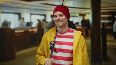 Çizgili gömlekli ve sarı ceketli mutlu bir adam otel lobisinde duruyor, rahat bir şekilde gülümsüyor, ev içi temalı eşsiz bir ortam yakalıyor..