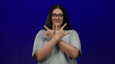 Gözlüklü kadın gülümsüyor ve mavi arka plana taş el hareketi yapıyor..