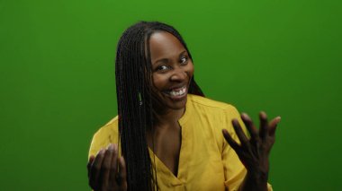 Sarı tişörtlü, örülmüş saçlarıyla yeşil duvara gülümseyen kadın, etkileyici ve karizmatik varlık izole arkaplan düzenine canlılık ve pozitiflik katıyor.