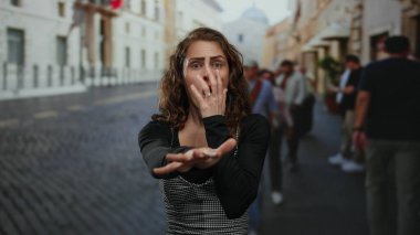 Arka planda bulanık yayalar ve motosikletle dolup taşan şehir caddesinde yüzü korkuyla korunan bir kadın..