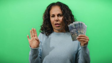 Güney Afrika banknotlarını elinde tutan orta yaşlı bir kadın izole edilmiş yeşil arka plan duvarına karşı şaşırmış bir ifadeyle para birimi ve ekonomik kavramları vurguluyor..