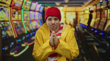 Parlak ceketli ve bereli genç adam renkli kumar makineleriyle dolu aydınlanmış kumarhanenin içinde umut dolu bir ifadeyle duruyor..