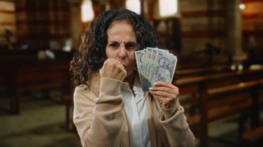 Orta yaşlı bir kadın Romen banknotlarını elinde tutuyor, kilise ortamında yumruğuyla bir jest yapıyor, meydan okuma veya kararlılığını dile getiriyor..