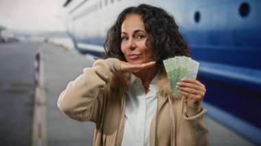 Orta yaşlı bir kadın arka planda teknesi olan bir sahil limanında Romanya banknotları tutuyor ve açık havada deniz kenarında rahat bir atmosfer yakalıyor..