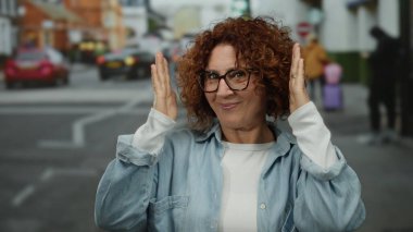 Hareketli bir şehir caddesinde elleri ile çerçeveleme kadın, orta yaş, açık hava düzeni ve canlı kentsel yaşam özünü yakalıyor.