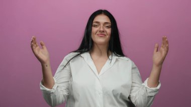 Büyük beden bir kadın, beyaz gömlekli, elleri pembe arka planda, kendine güveni ve zarafeti canlı bir ortamda somutlaştırıyor..