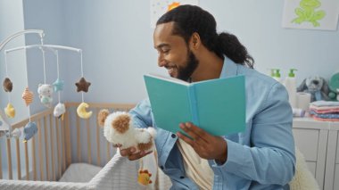 Adam, oyuncaklarla çevrili, rahat bir yatak odasında bebeğe kitap okuyor, evde sıcak ve besleyici bir ortam yaratıyor..