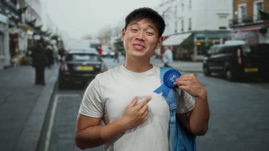 Genç bir adam gururla mavi bir kurdeleyi şehir sokaklarında sergiliyor, neşeli bir öğrenci havasını somutlaştırıyor..