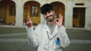 Laboratuvar önlüğü giyen İspanyol genç adam eski bir üniversite ortamında özgüvenle gülümsüyor akademik coşkuyu somutlaştırıyor ve entellektüel bir ortam yakalıyor..