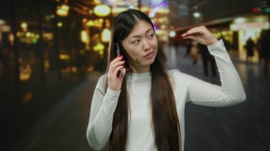 Şehir caddesinde gece vakti, arka planda bulanık ışıklarla şakacı hareketler yapan bir kadın telefonda konuşuyor..