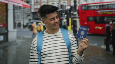 Elinde Kore pasaportu olan, arka planda kırmızı otobüsü olan, çizgili ve mavi sırt çantalı bir adam gülümsüyor..