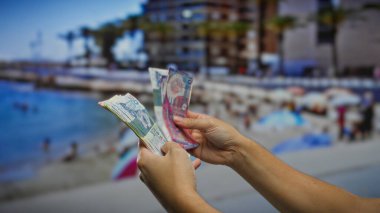 Deniz kenarında Hong Kong dolarlarının banknotlarını tutan adam, canlı bir şehir ortamında yaz tatilini, yatırım fırsatlarını ve döviz kurunu vurguluyor..