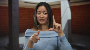 Çinli bir kadın, neşeli bir ifade ve rahat bir duruş ile bir inşaat alanında neşeli bir şekilde el kol hareketi yaparak, neşeli bir etkileşim anını yakalıyor..