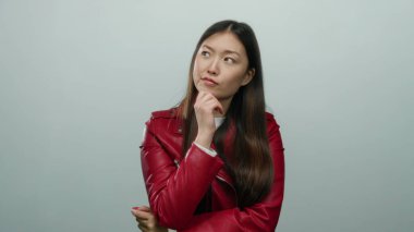 Beyaz bir arkaplan üzerinde düşünceli bir kadın, uzun siyah saçlı kırmızı bir ceket giyiyor, tefekkür ve ifade sergiliyor.