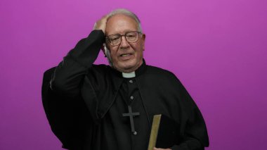 Siyah cüppeli kıdemli rahip, elinde bir kitap, pembe bir arka plan üzerinde duruyor, düşünceli bir ifadeyle, inancı ve düşünmeyi ön plana çıkarıyor..