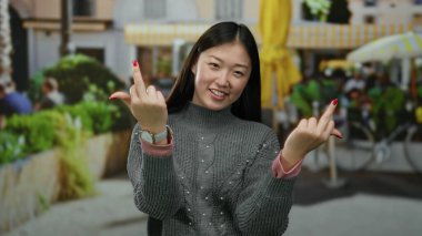 Kadın, şehir ortamında şakacı bir ifadeyle mizahi bir şekilde hareket eder, günlük bir süveter giyer, şehir hayatı ve canlı yeşilliklerle çevrilidir, gün boyunca..