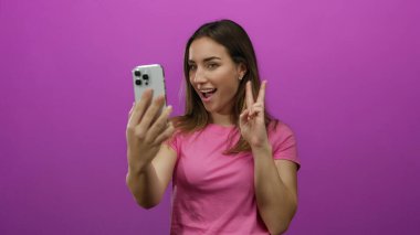 Pembe arka planda akıllı telefonlu selfie çeken bir kadın barış işareti yapıyor. Sarışın, izole edilmiş, mutlu, sıradan teknoloji modern portre..