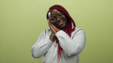 Afro-Amerikalı bir kadın sarı arka plan duvarında uyuyor gözleri kapalı ve elleri beyaz kıyafetler ve pembe örgülerle birlikte..