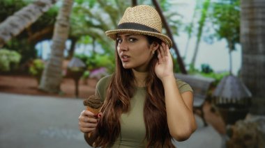 Şapkalı kadın, ağaçlı parkta dondurma külahı tutuyor. Kafa karışıklığı ya da tatminsizliği ifade ediyor..