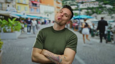 Şehir sokaklarında genç bir adam, canlı bir şehir arka planında mutluluk ve oyunculuğu ifade ederken dövmeleri ve kolları çaprazlanmış bir şekilde güvenle poz veriyor..