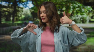 Neşeli bir açık hava parkı ortamında olumlu ve olumsuz duyguları ifade eden bir kadın. Karışık duygular, bir gülümseme ve güneş ışığı altında düşünceli bir ifade sergiliyor..