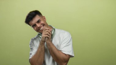 Gülümseyen adam yeşil arka plana karşı kulaklık ve beyaz gömlek takıyor. Dostça ve rahat bir duruş sergiliyor.