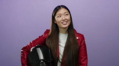 Stüdyoda kaskını tutarak gülümseyen bir kadın zarif kırmızı ceketiyle modern yaşam tarzını aktaran münferit mor arka plana karşı..