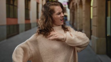 Kazaklı bir kadın şehir caddesinde acıdan suratını buruşturuyor. Rahatsızlığını ifade ediyor ve gergin bir ifadeyle omzunu tutuyor. Şehir hayatını ve sağlık sorunlarını gösteriyor..