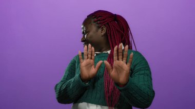 Afro-Amerikalı bir kadın cesur, mor izole bir geçmişe karşı reddedilmiş bir jestle onaylamadığını belirterek otantik duygular ve canlı moda seçimleri sergiliyor..