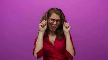 Dışlanmış pembe bir arka plan duvarından tiksinen bir kadın. Gözlüklü, yüz ifadeleriyle duygularını gösteren negatif duygular taşıyan bir kadın..