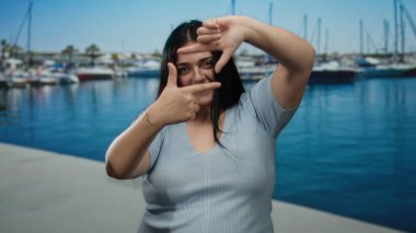 Kadın arka planda teknelerle deniz kenarında neşeli bir şekilde poz veriyor, neşeli, açık hava atmosferini somutlaştırıyor.