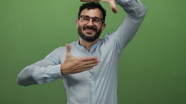 Sakallı ve mavi gömlekli İspanyol bir adam yeşil arka plana karşı yüzünü çerçeveliyor, yaratıcılık ve ifade aktarıyor..