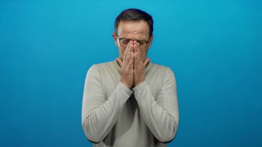 Gözlüklü İspanyol bir adam mavi arka planda duruyor. Elleri yüzü üzerinde, dışlanmış bir ortamda stres ya da hayal kırıklığı gösteriyor. Duygularını ve iç gözlemlerini aktarıyor..