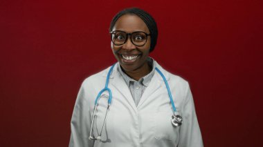 Beyaz önlüklü ve steteskoplu gülümseyen kadın kırmızı duvara dayanmış mutlu profesyonel doktor konseptini gösteriyor.