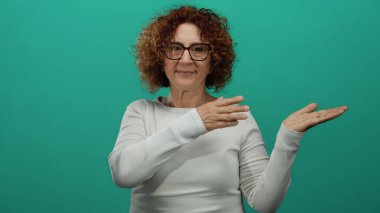 İzole edilmiş yeşil arka planı olan, elleri açık, esmer, doğrudan bakan, beyaz uzun kollu gömlek giyen, dışavurumcu jestleri vurgulayan bir kadın..