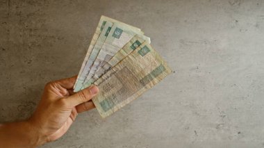 Adamın eli, somut bir arkaplan karşısında birkaç Mısır sterlini banknotunu tutarak mali bağlam ve kültürel para birimi unsurlarını vurguluyor..