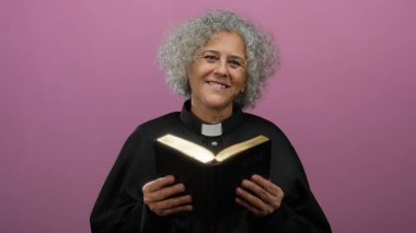 Gri saçlı kadın rahip pembe arka planda İncil okuyor..