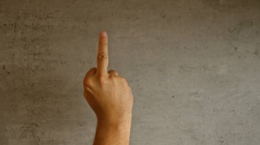 Adamın eli, arka planda gri beton duvara parmak gösteriyor. Karşı gelme ya da onaylamama hareketi..
