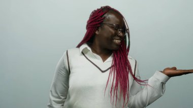 Örgülü saçlarıyla gülümseyen kadın, izole edilmiş stüdyo ortamında beyaz arka planda sunum ya da davet konsepti sunan elini uzatıyor