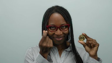 Gözlüklü Afrikalı Amerikalı bir kadın beyaz bir duvara monero bozuk para tutuyordu. Sanal para konsepti sergiliyordu. Kendine güvenen bir ifadesi ve profesyonel kıyafeti vardı..