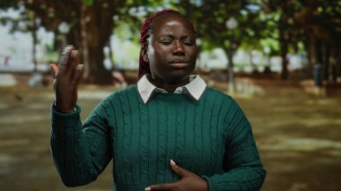 Afrika kökenli Amerikalı bir kadın, elini güneşli bir park ortamında serinleterek, yemyeşil ağaçların gölgesinde açık hava sıcağından kendini kurtarıyor..