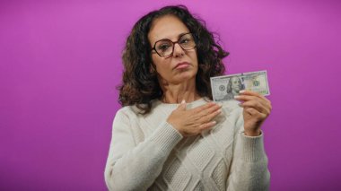 Elinde 100 dolarlık banknot tutan orta yaşlı bir kadın, göğsünde parlak bir mor arkaplan olduğunu gösteriyor. Bu da para ve kendini tanıtma arasında bir bağlantı olduğunu gösteriyor..