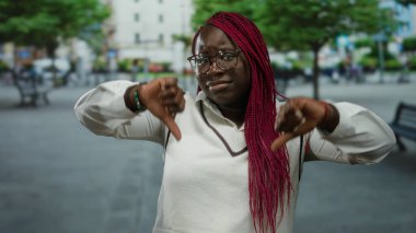 Arka planda ağaçlar ve binalar olan bir şehir caddesinde şehir yaşamını ve duygularını sergileyen bir kadın tasvip etmiyor..