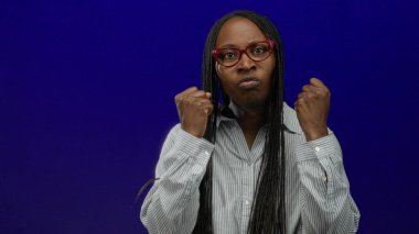 Gözlüklü ve örgülü bir kadın öfkesini mavi duvara yumruk atarak ifade ediyor. Duygularını ve gücünü sergiliyor..