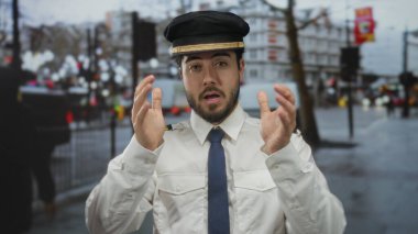 Kılavuz üniformalı, sakallı genç bir adam işlek bir sokak arka planında profesyonellik ve seyahat atmosferini aktarıyor..